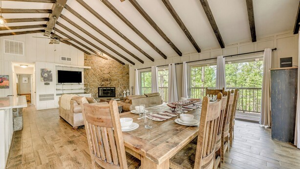 Ein geräumiger Essbereich mit Holztisch und -stühlen, einem Steinkamin und großen Fenstern mit Blick ins Freie.