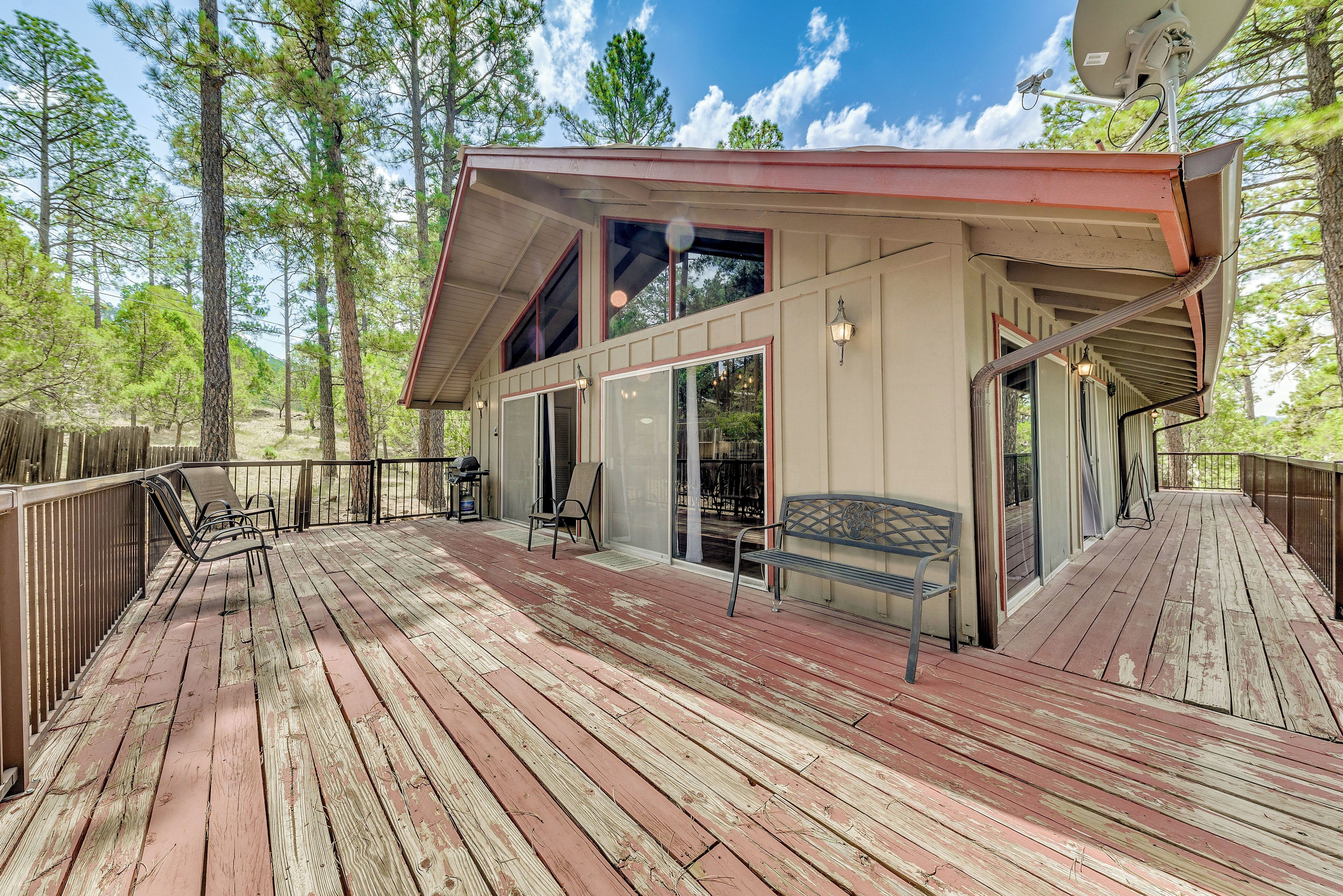 A wooden deck with outdoor furniture, a covered patio, and a view of a forested area.