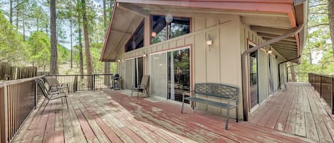 A wooden deck with outdoor furniture, a covered patio, and a view of a forested area.