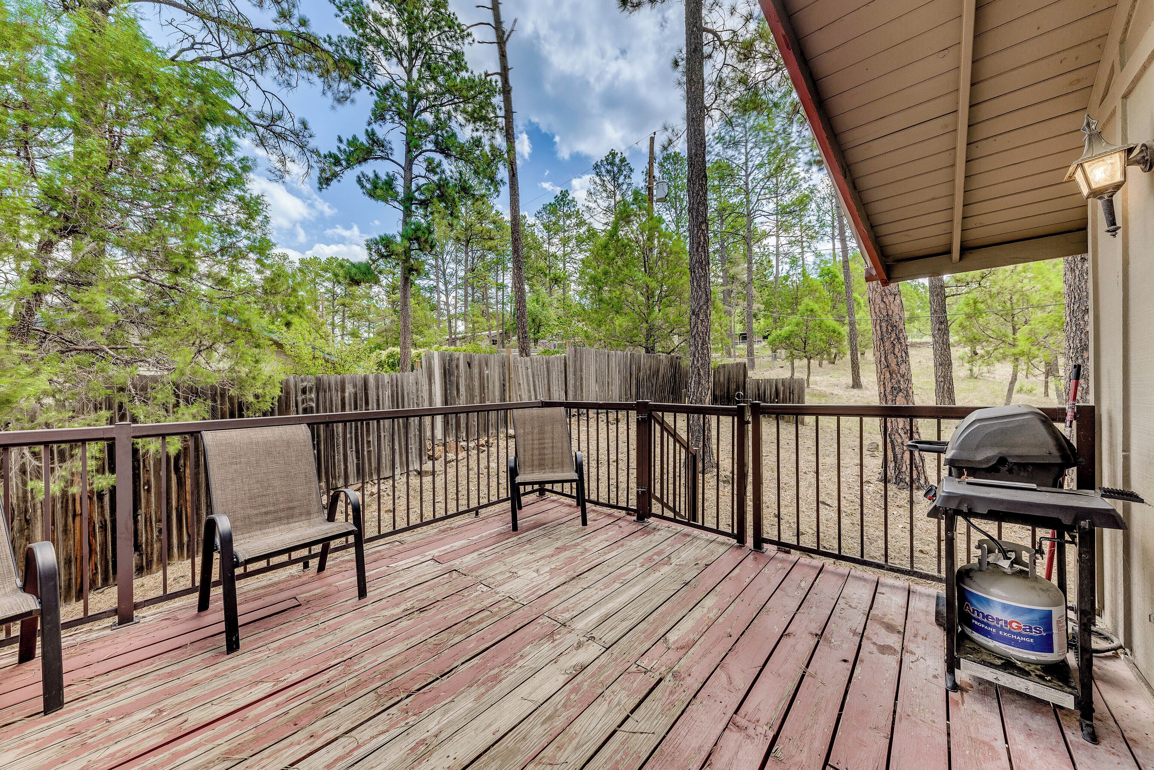 A wooden deck with two chairs, a grill, and a propane tank.