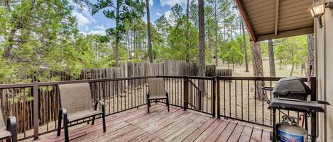A wooden deck with two chairs, a grill, and a propane tank.