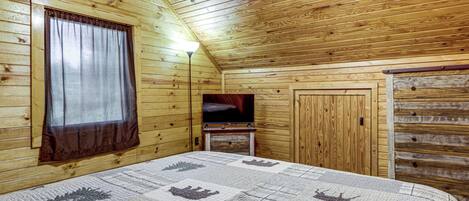 A wooden cabin room with a bed, a television, and a wardrobe.