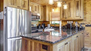 A kitchen with wooden cabinets, stainless steel appliances, granite countertops, and pendant lighting. - Views, Fire Pit + Game Room: Smoky Mountain Cabin (Sevierville)