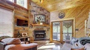 A cozy cabin interior with a stone fireplace, leather furniture, and a wooden ceiling. - Views, Fire Pit + Game Room: Smoky Mountain Cabin (Sevierville)