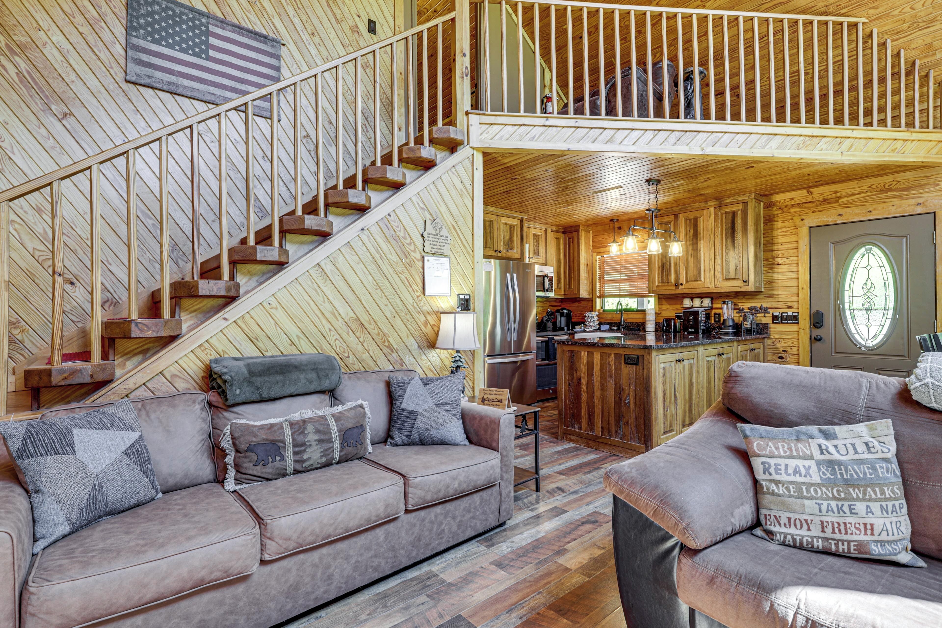 L’intérieur d’une cabane comprend un escalier en bois, un coin cuisine, un salon avec un canapé et un balcon situé à l’étage.