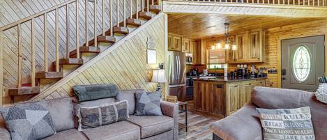 L’intérieur d’une cabane comprend un escalier en bois, un coin cuisine, un salon avec un canapé et un balcon situé à l’étage.