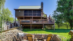 A two-story wooden house with a stone patio, outdoor seating, and a grill. - Views, Fire Pit + Game Room: Smoky Mountain Cabin (Sevierville)