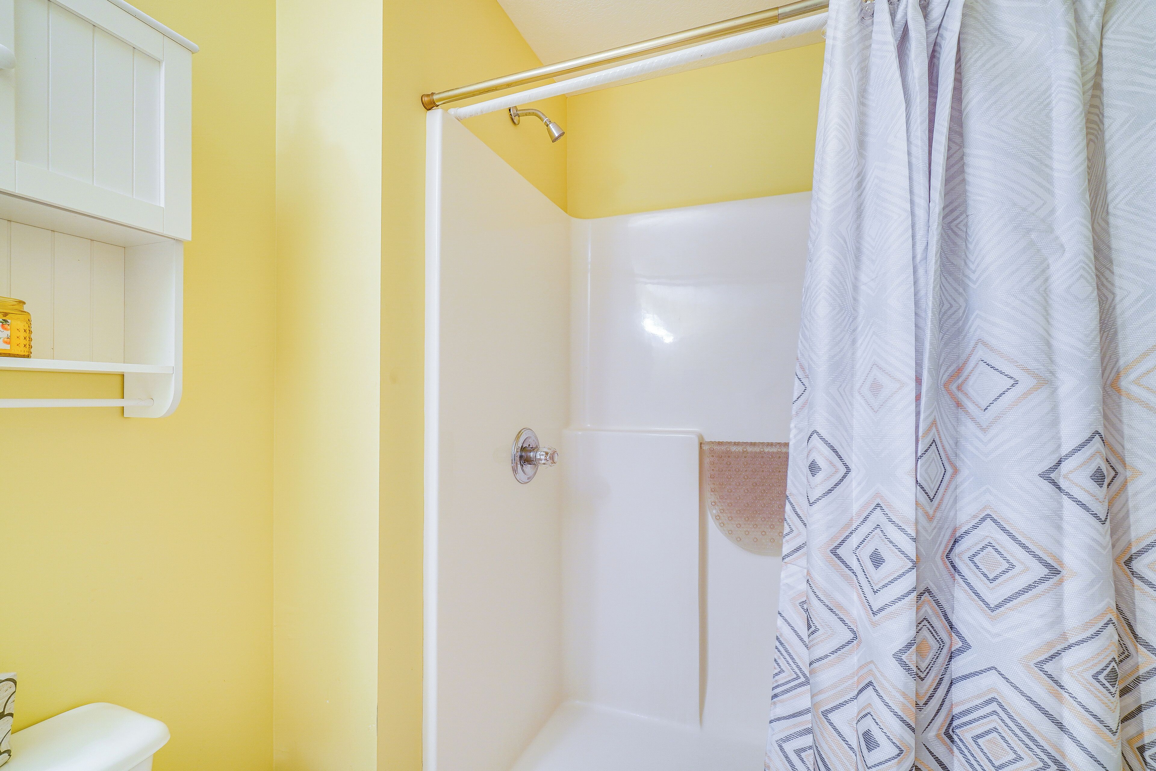 Un baño con ducha, inodoro y estante con artículos de aseo.
