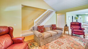 A living room with a beige sofa, red armchairs, a patterned rug, and a staircase with white railings. - Pigeon Forge Home w/ Deck & Hot Tub Near Town! (Pigeon Forge)