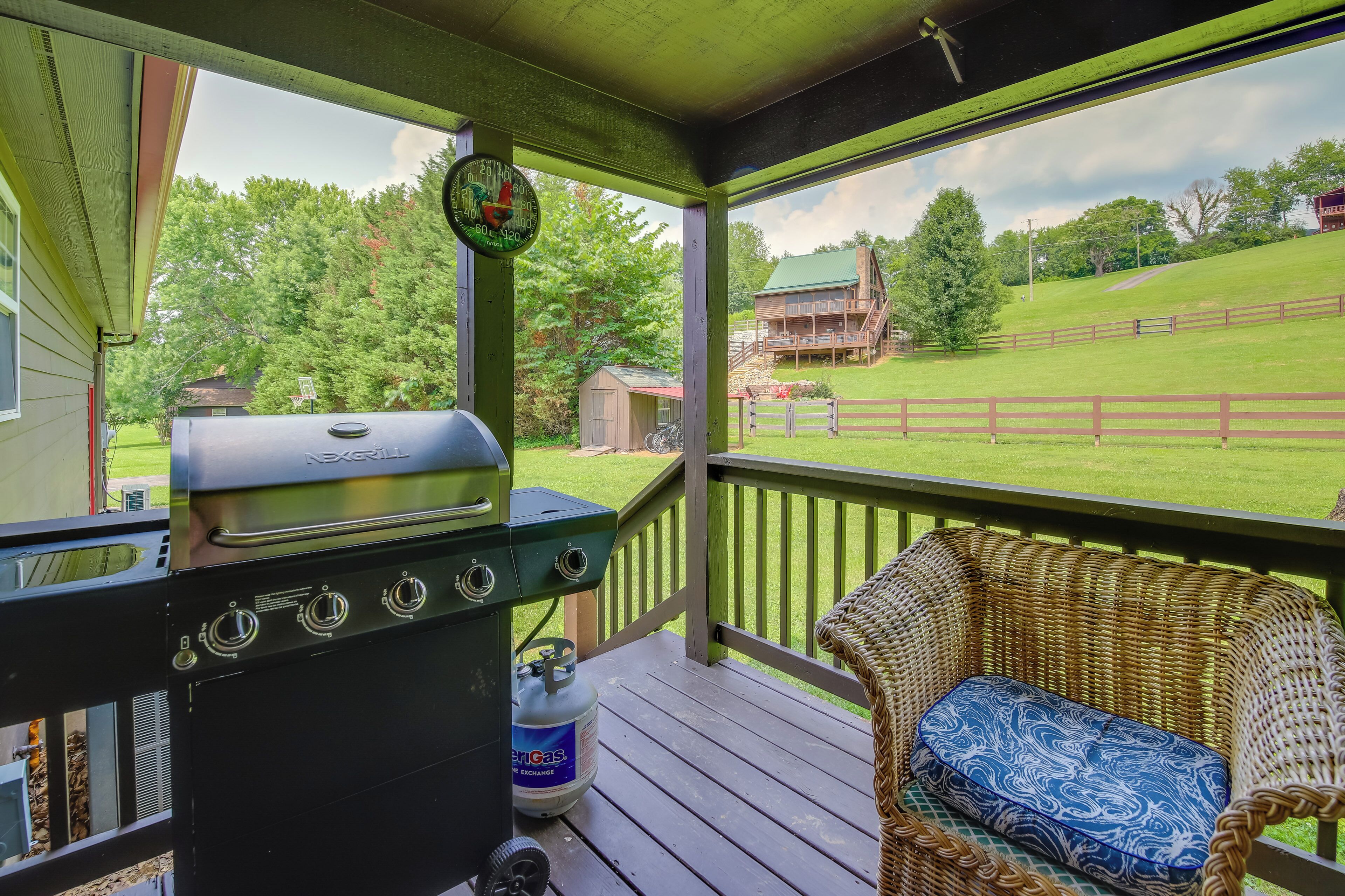 A covered outdoor area with a grill, a wicker chair, and a view of a house and yard.
