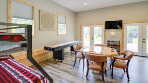 Une pièce avec des lits superposés, une table de billard, une table à manger avec des chaises et un téléviseur fixé au mur.