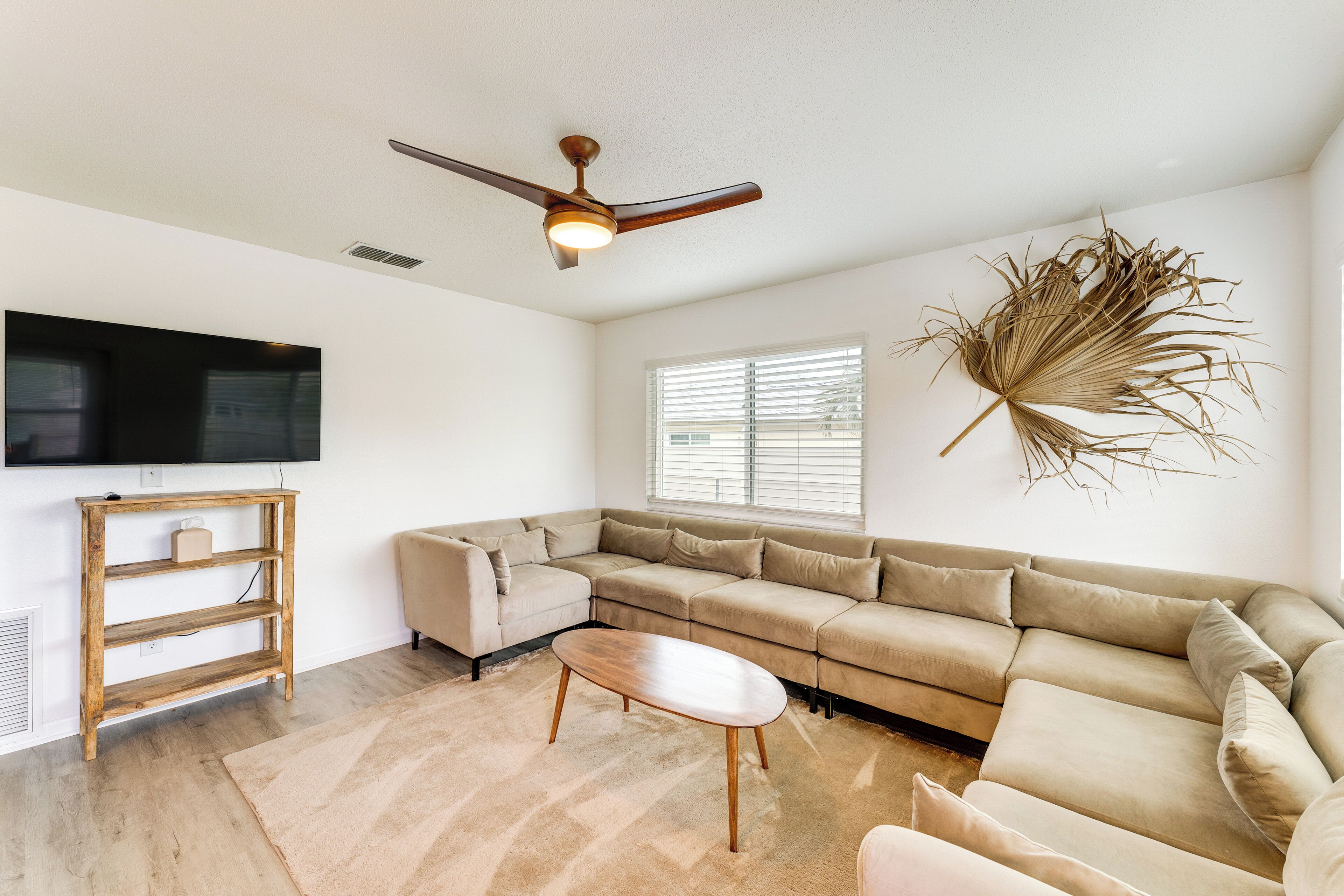 A living room with a sectional sofa, a wooden coffee table, a TV on a stand, and a ceiling fan.
