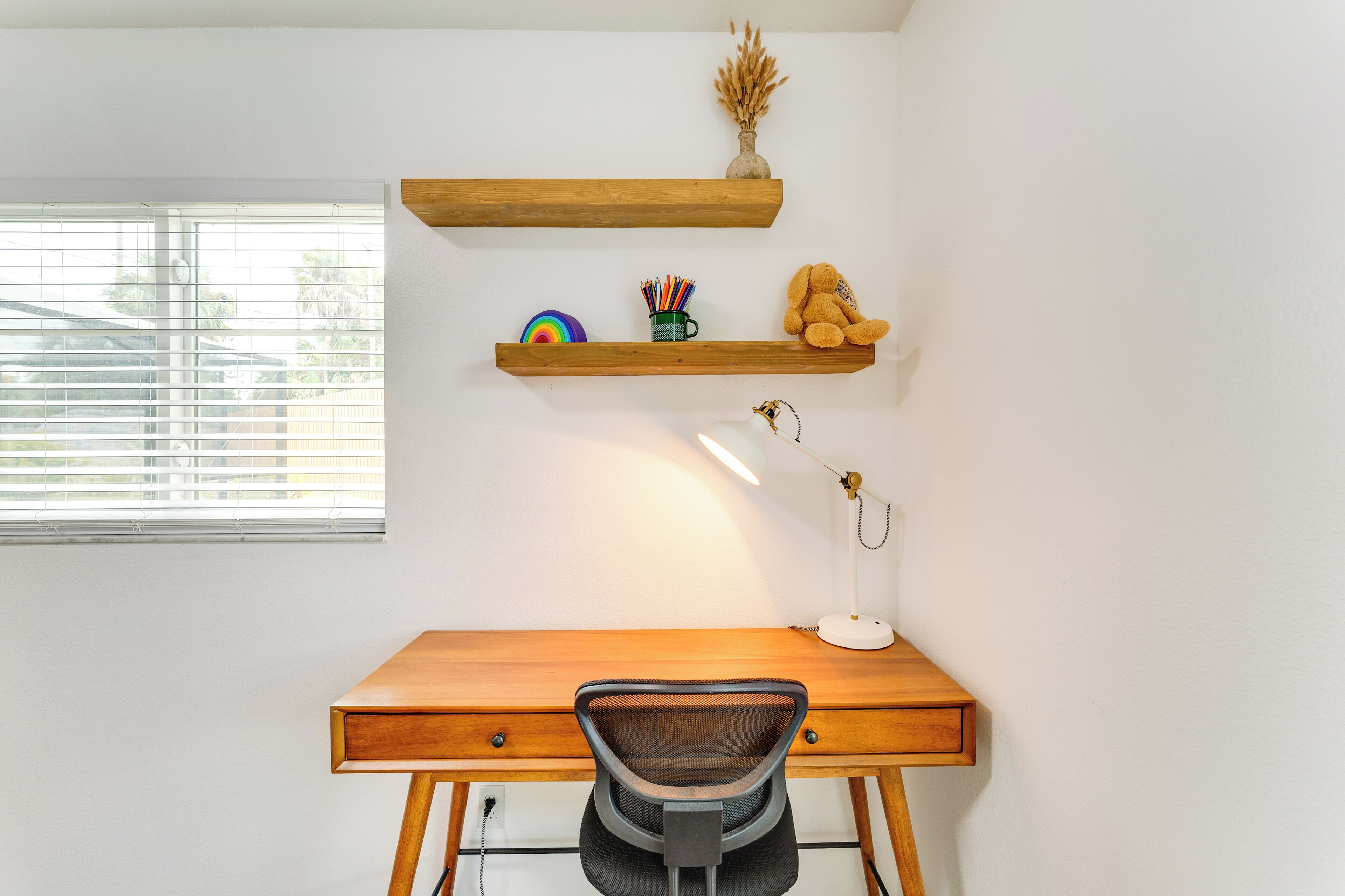 A wooden desk with a chair, a lamp, and two shelves with decorative items.