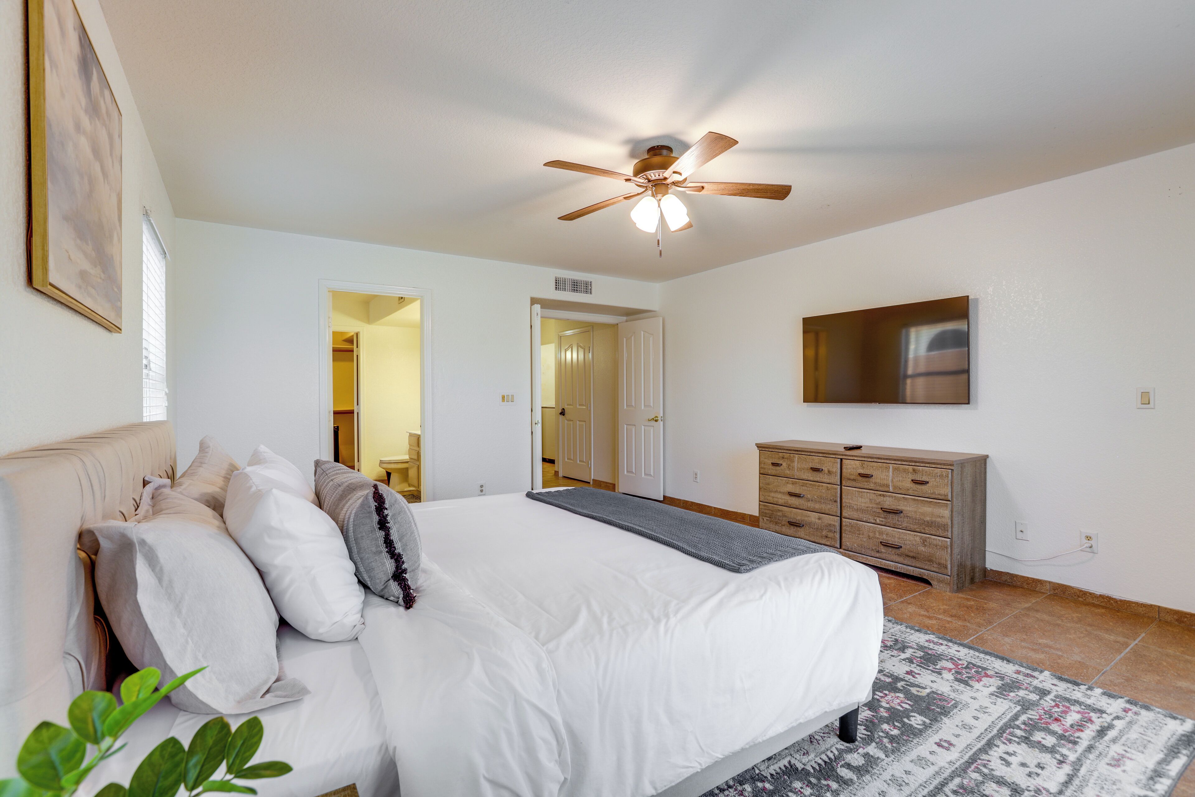 A bedroom with a bed, a dresser, a ceiling fan, and a door leading to another room.