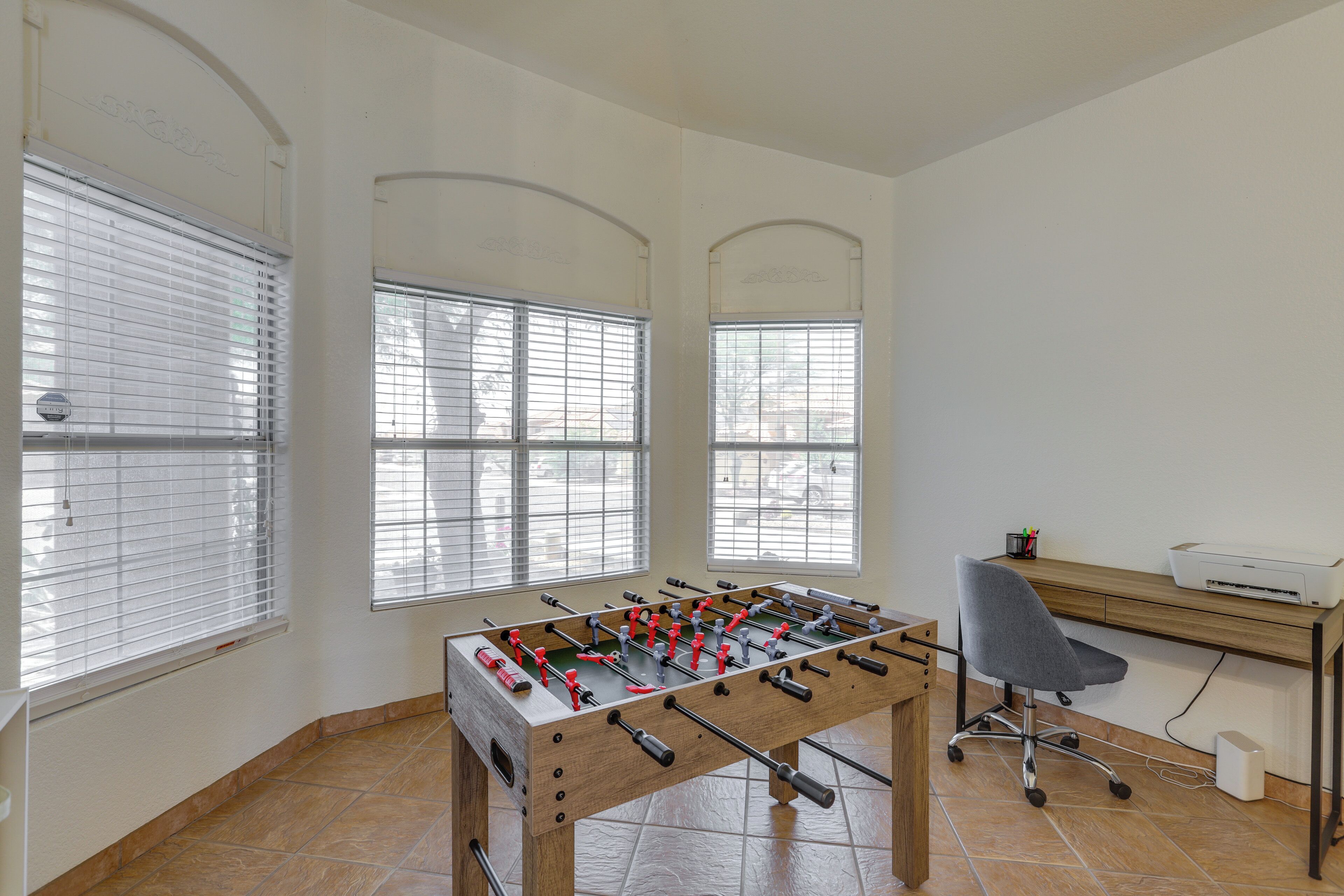 A room with a foosball table, a desk with a printer, and a chair.