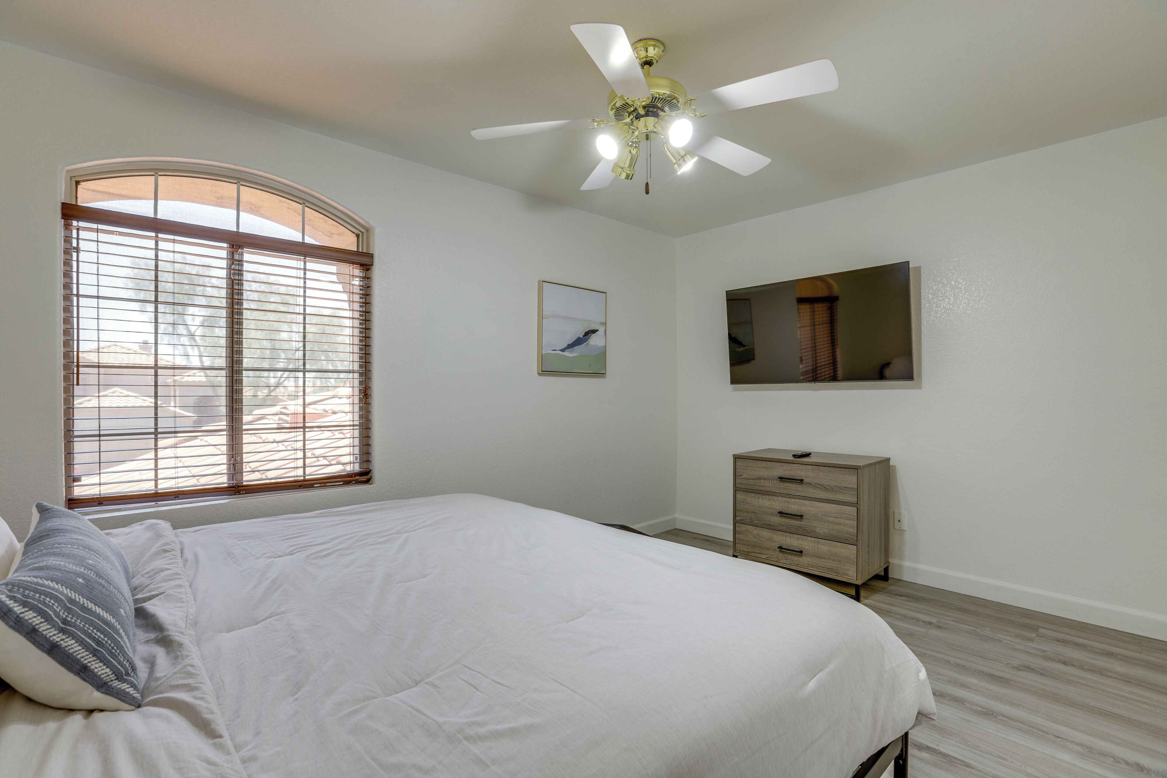 A bedroom with a bed, a dresser, a ceiling fan, a window with blinds, and a framed picture on the wall.