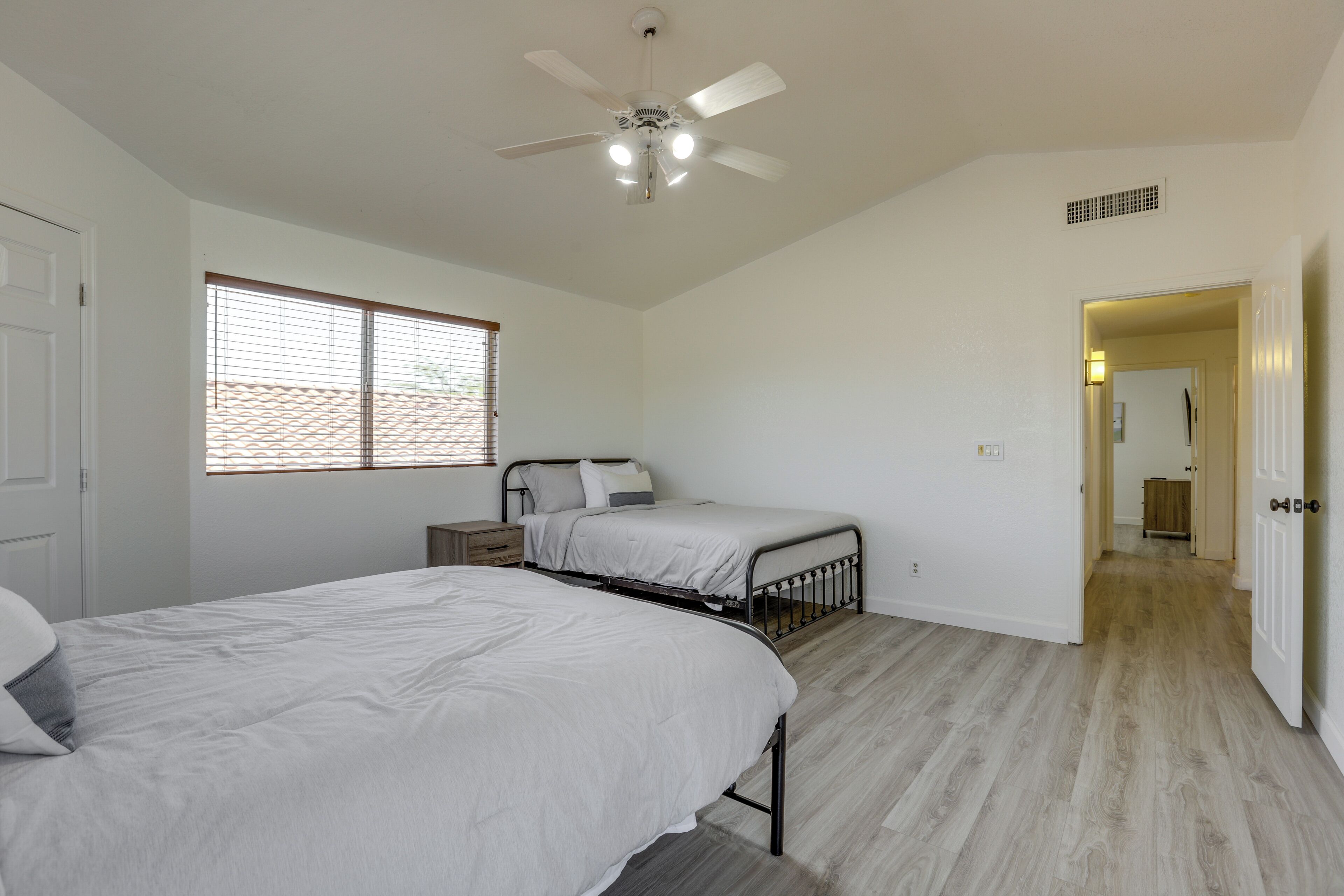 A bedroom with two beds, a ceiling fan, and a window with blinds.