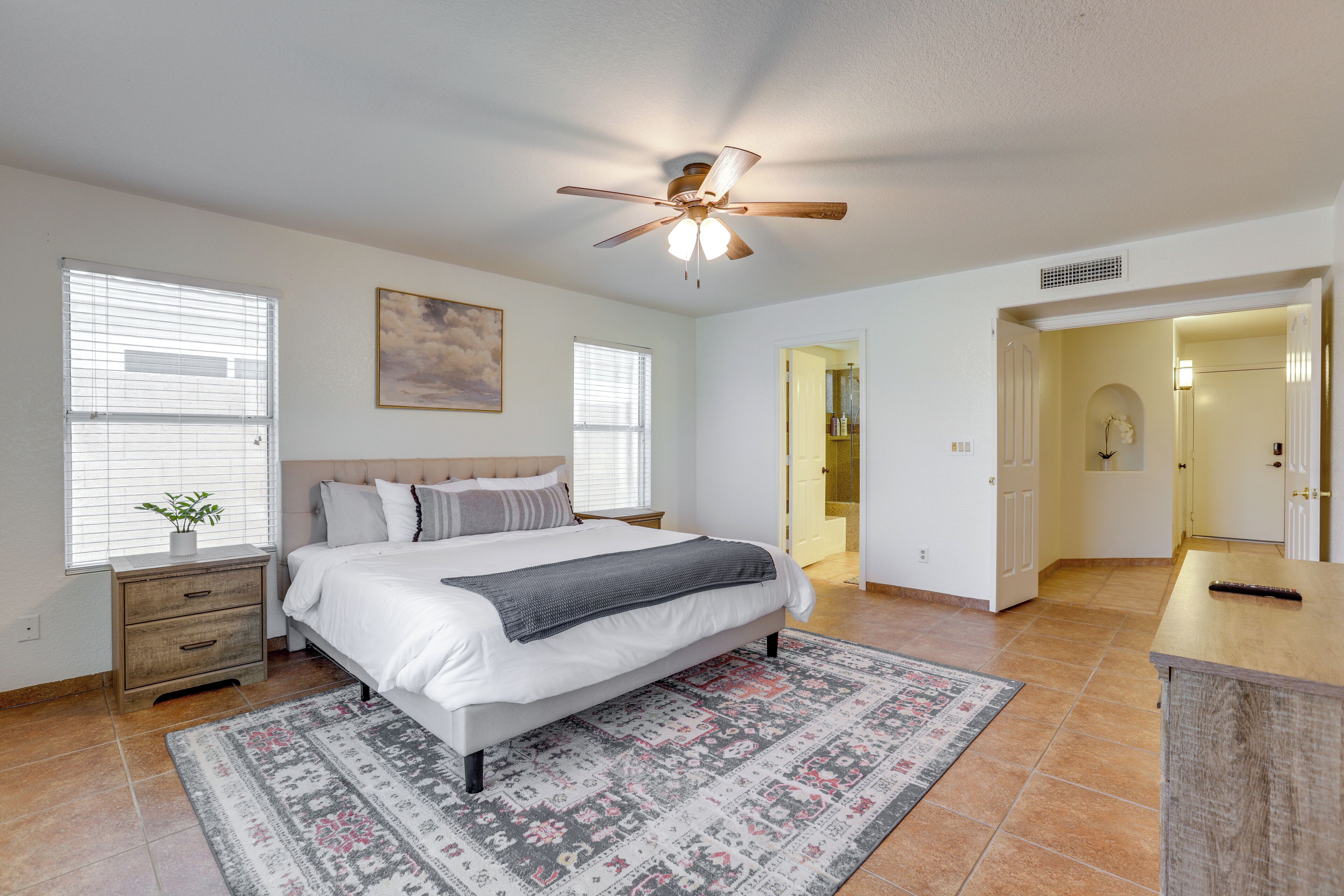 A bedroom with a bed, bedside tables, a ceiling fan, and a patterned rug.