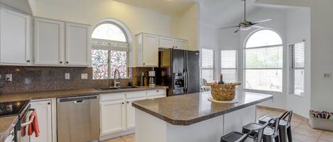 A spacious kitchen with white cabinets, a granite countertop, and a central island with bar stools.