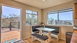 A room with a bench seating area, a small table with a vase, and large windows offering a view of trees and hills. - Oakhurst Duplex ~ 13 Mi to Yosemite National Park! (Oakhurst)