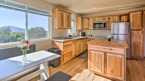 A modern kitchen with wooden cabinets, stainless steel appliances, and a large window offering a view of the outdoors. - Oakhurst Duplex ~ 13 Mi to Yosemite National Park! (Oakhurst)