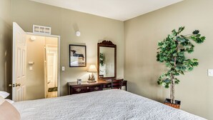 Quarto com cama grande, penteadeira, espelho, abajur e planta em vaso.