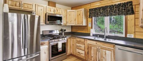 A modern kitchen with wooden cabinets, stainless steel appliances, and a large window with a view of trees.