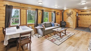 A cozy cabin interior with a dining area, sofa, and a fireplace. - Welcoming Wasilla Cabin w/ Patio! (Wasilla)