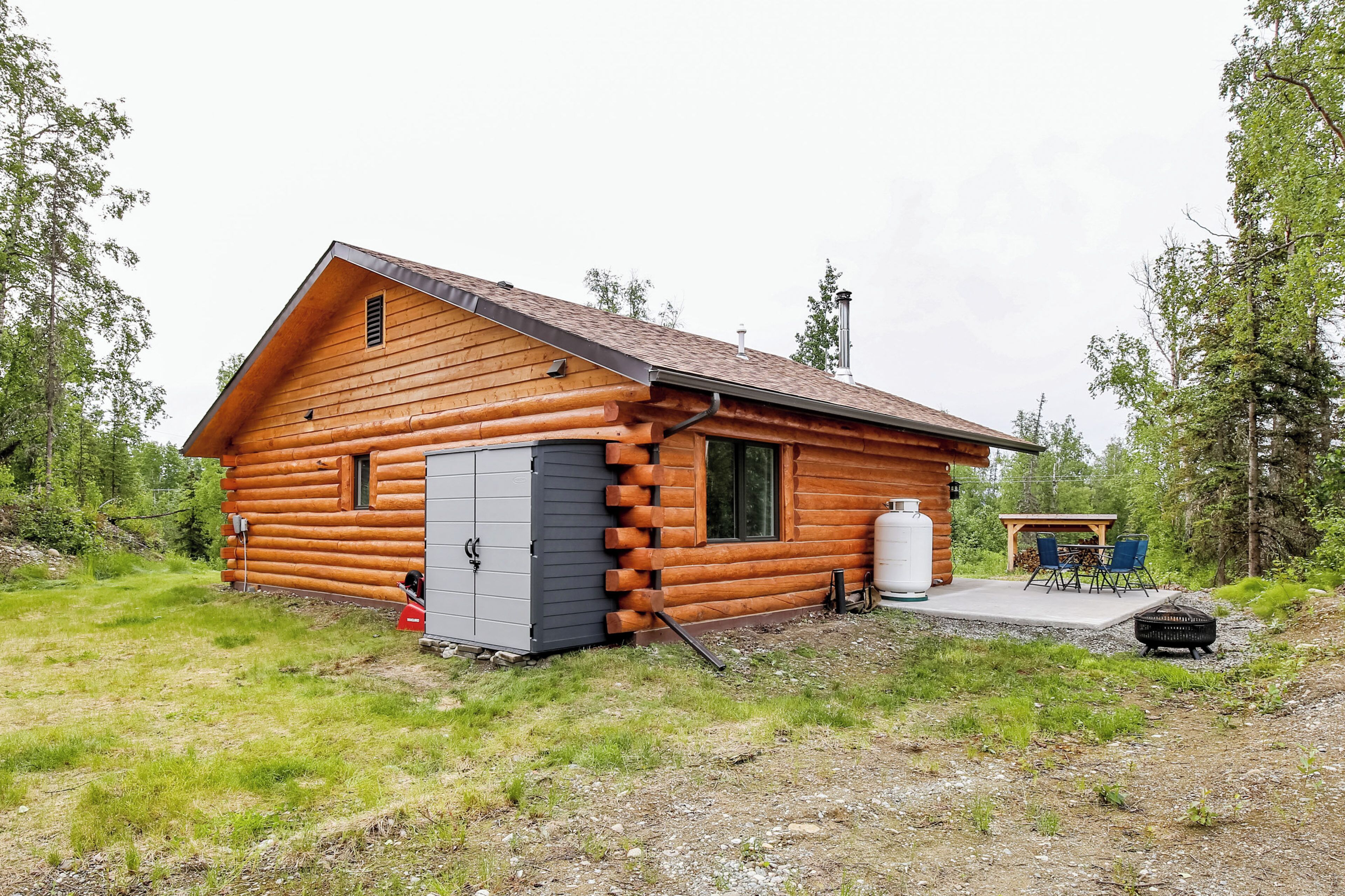 A log cabin with a porch, a water tank, and a grill area.