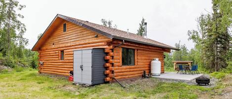 A log cabin with a porch, a water tank, and a grill area.