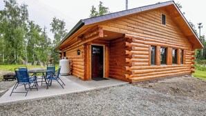 A log cabin with a porch, outdoor seating, and a chimney. - Welcoming Wasilla Cabin w/ Patio! (Wasilla)