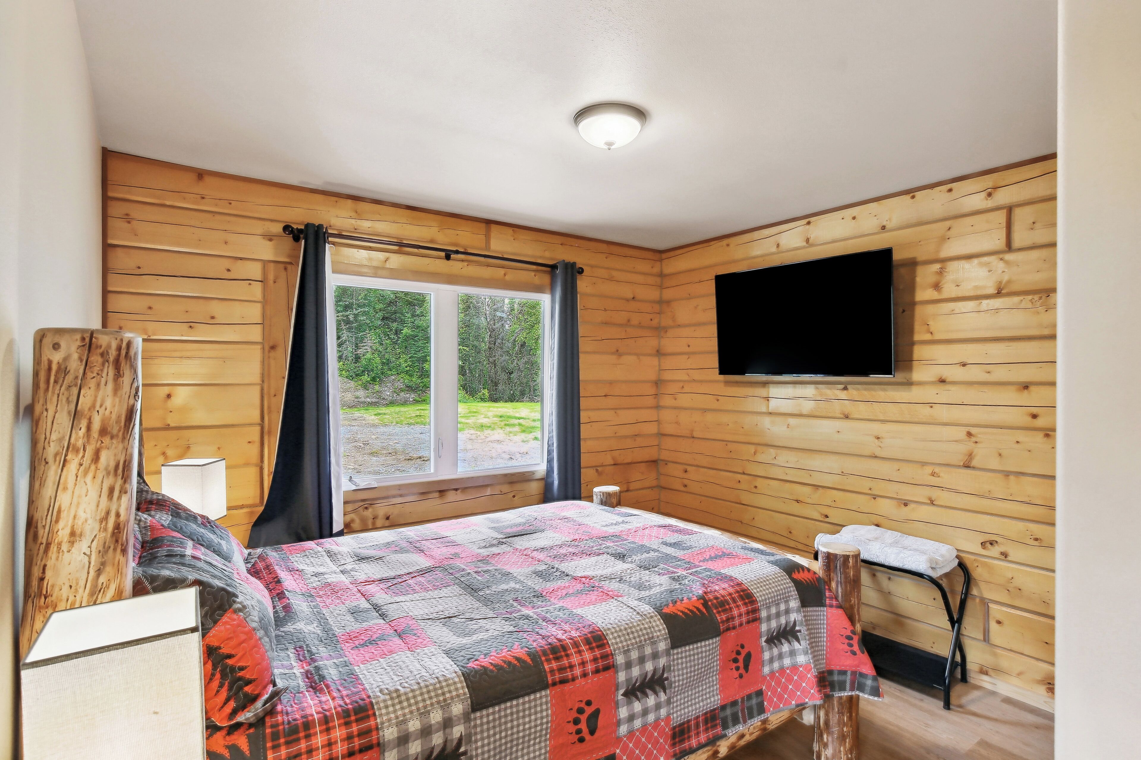 A wooden-paneled room with a bed, a TV mounted on the wall, and a window with curtains.