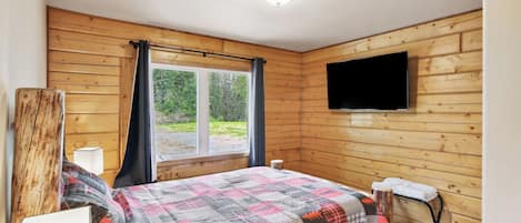 A wooden-paneled room with a bed, a TV mounted on the wall, and a window with curtains.