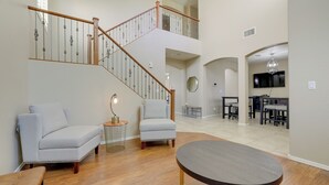 A spacious living area with a wooden staircase, two armchairs, a round table, and a dining area in the background.