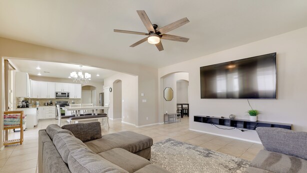 A spacious living area with a large sectional sofa, a flat-screen TV mounted on the wall, and a ceiling fan.