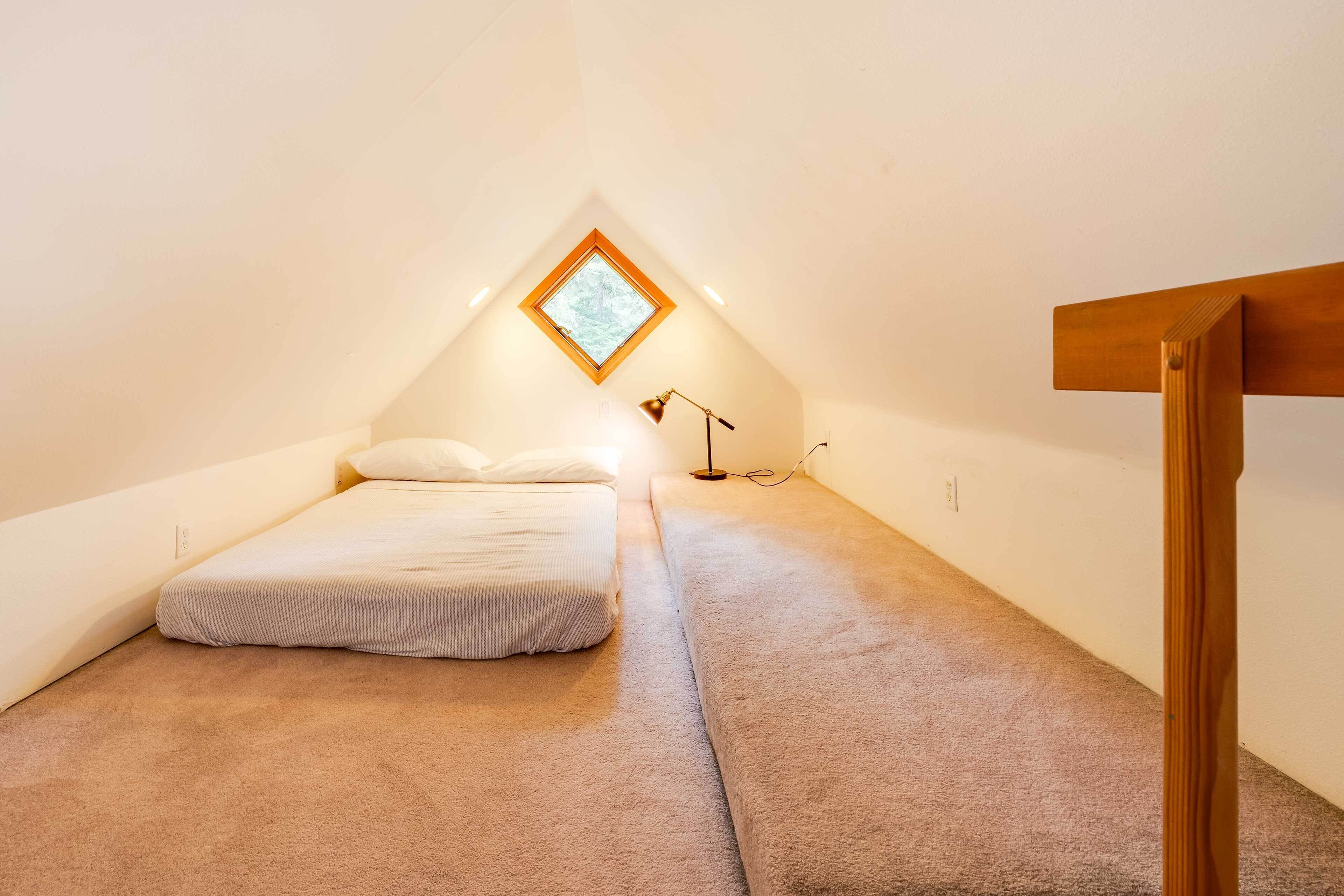 Une petite chambre mansardée, chaleureuse et accueillante, avec un plafond en pente, un lit simple, un bureau et une fenêtre.