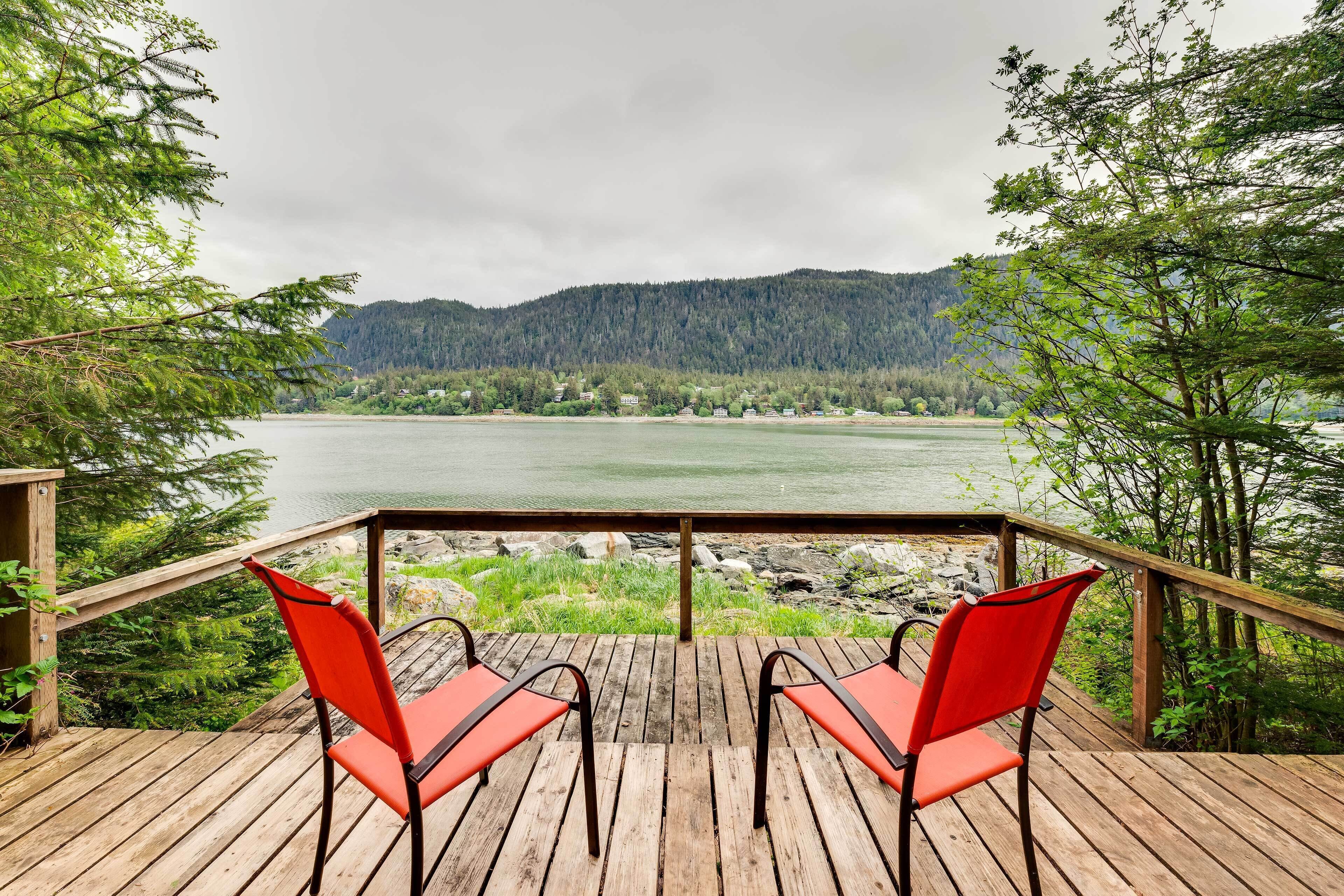 A wooden deck with two red chairs facing a lake and forested hills.