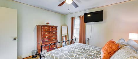 Un dormitorio con cama, ventilador de techo, cómoda, espejo y televisor montado en la pared.