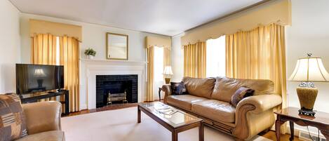 A living room with a leather sofa, a glass coffee table, a fireplace, and a television.