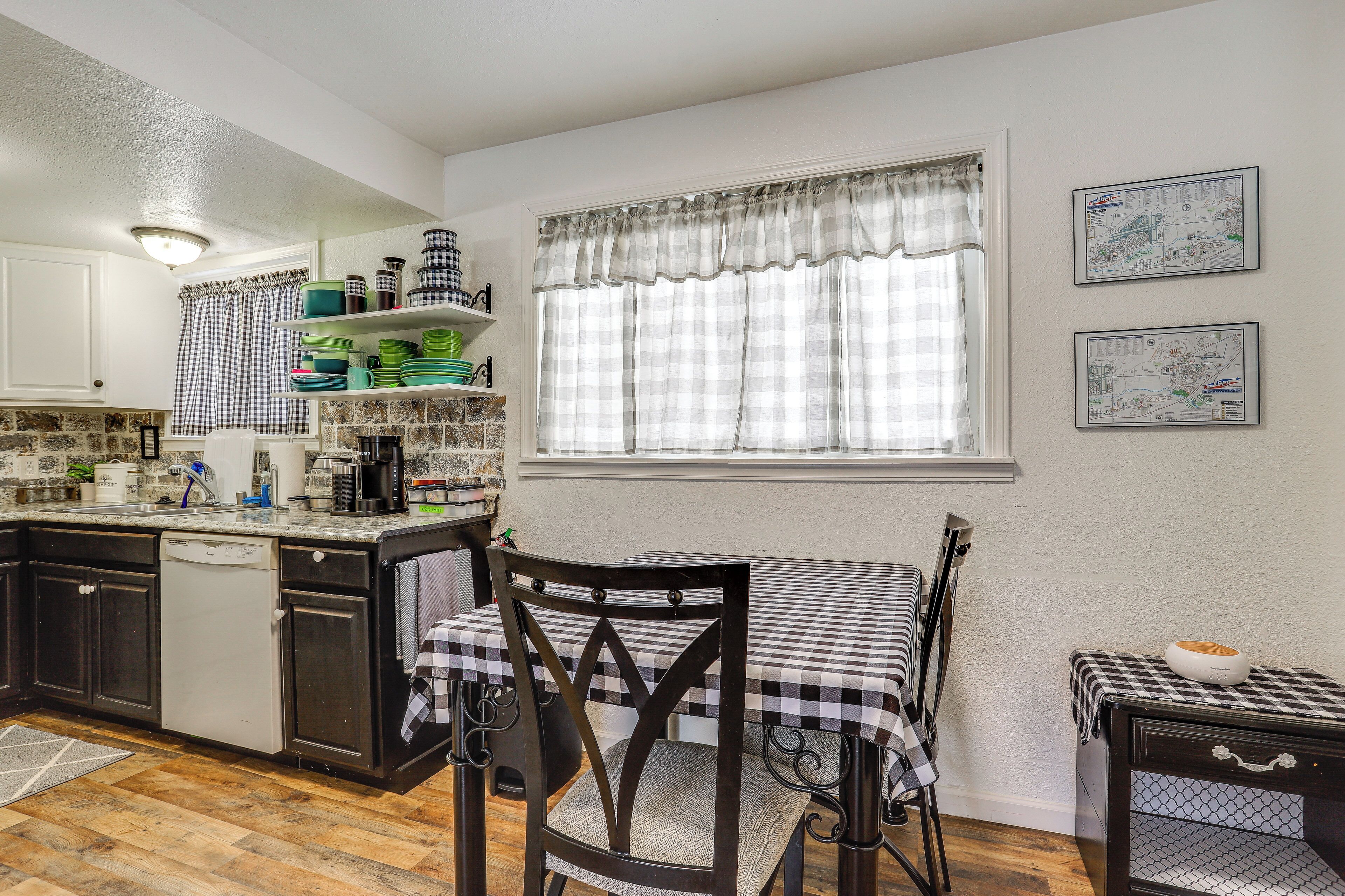 A kitchen with a dining table, chairs, a dishwasher, and a window with curtains.