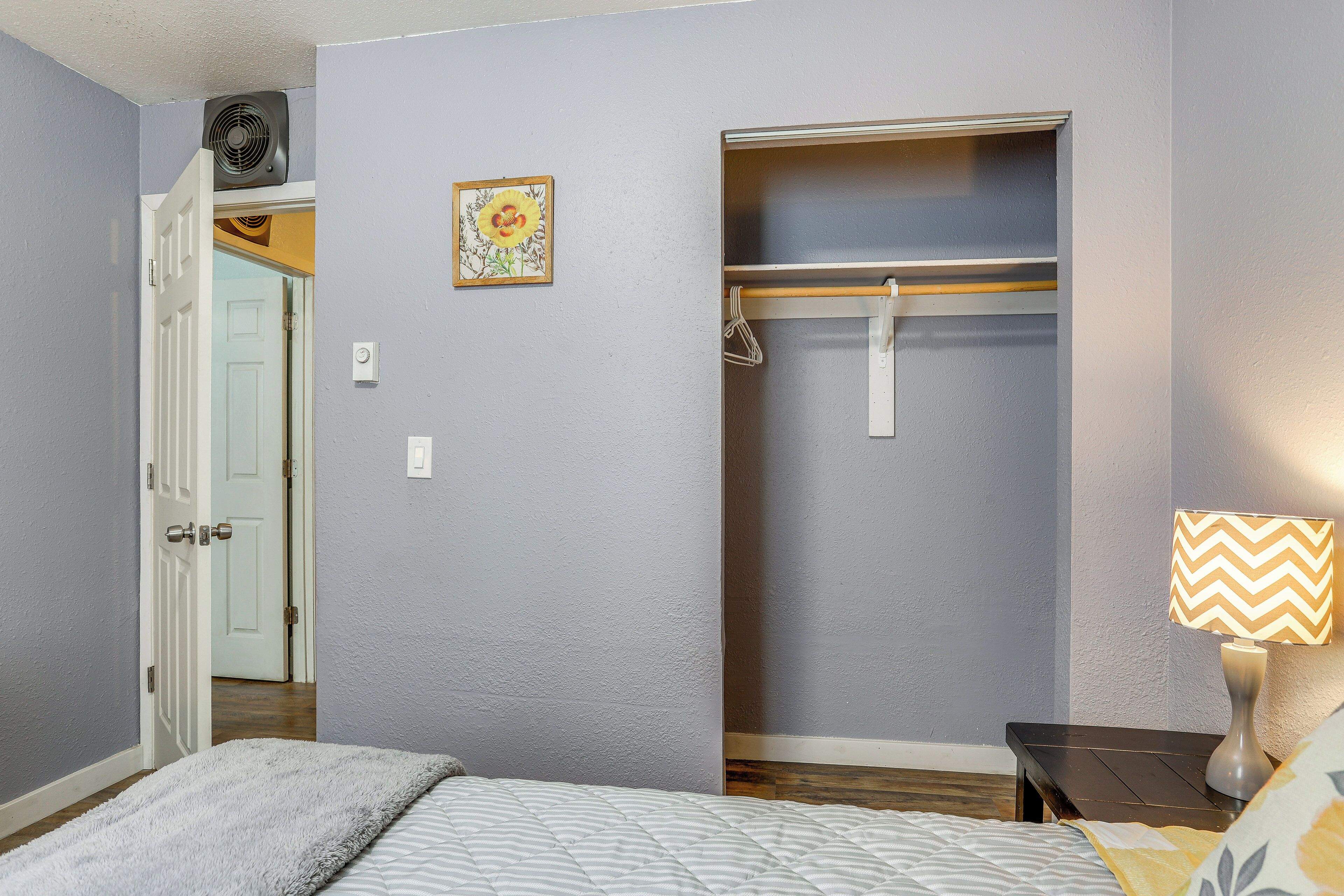 Een slaapkamer met een bed, een nachtkastje met een lamp, een kast met kledingroede en een deur naar een andere kamer.