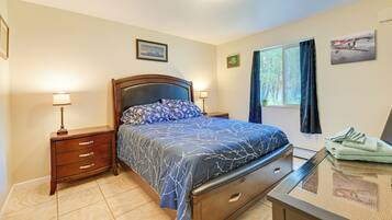 Quarto com cama, mesas de cabeceira, uma mesa e uma janela com cortinas.