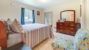 Ein Schlafzimmer mit einem Bett, einem Schminktisch, einem Sessel, einem Fenster mit Vorhängen und einer Tür.