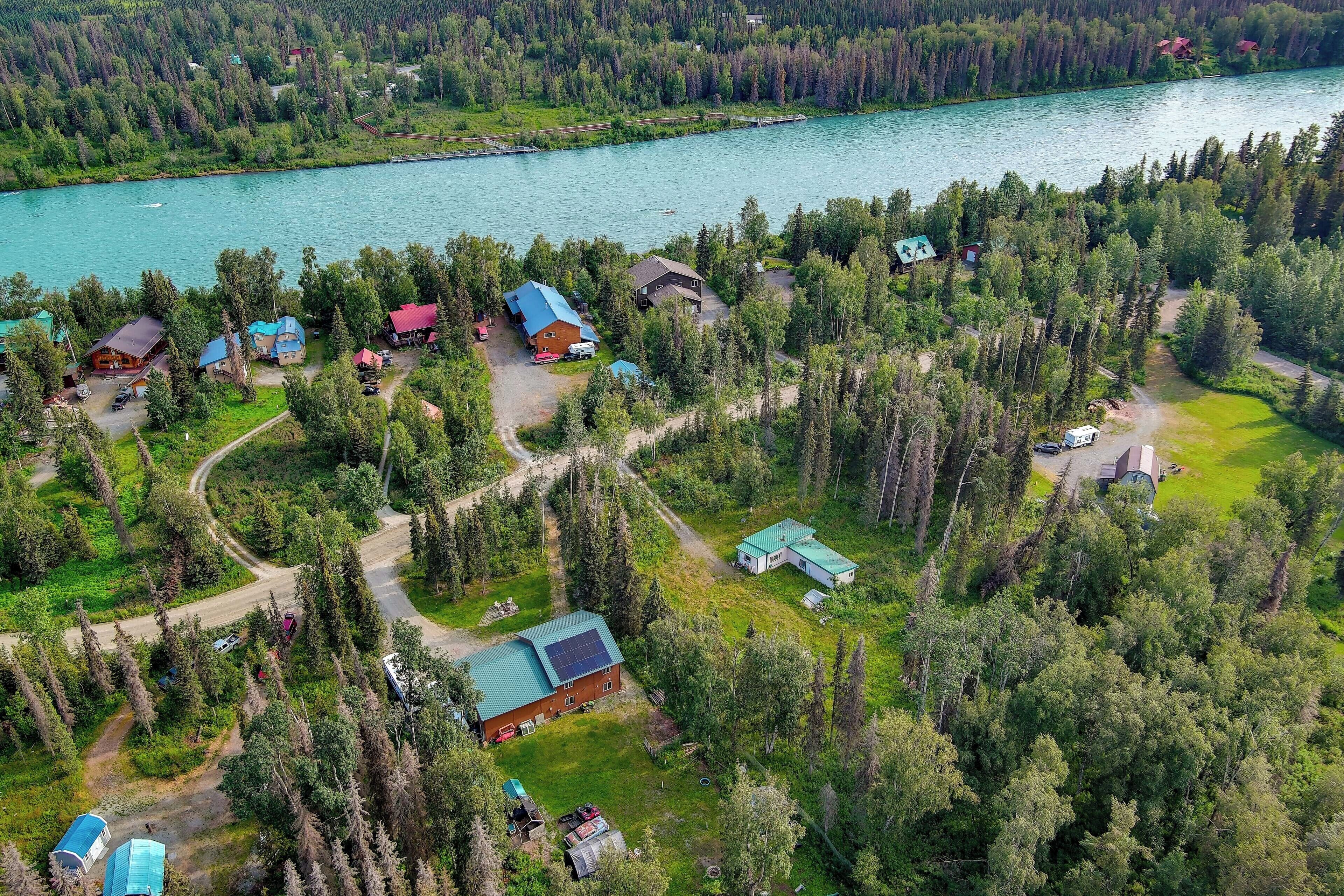 Vue aérienne d’un ensemble de chalets au bord d’un lac, composé de plusieurs bâtiments, entourés d’une forêt dense et traversés par une rivière.