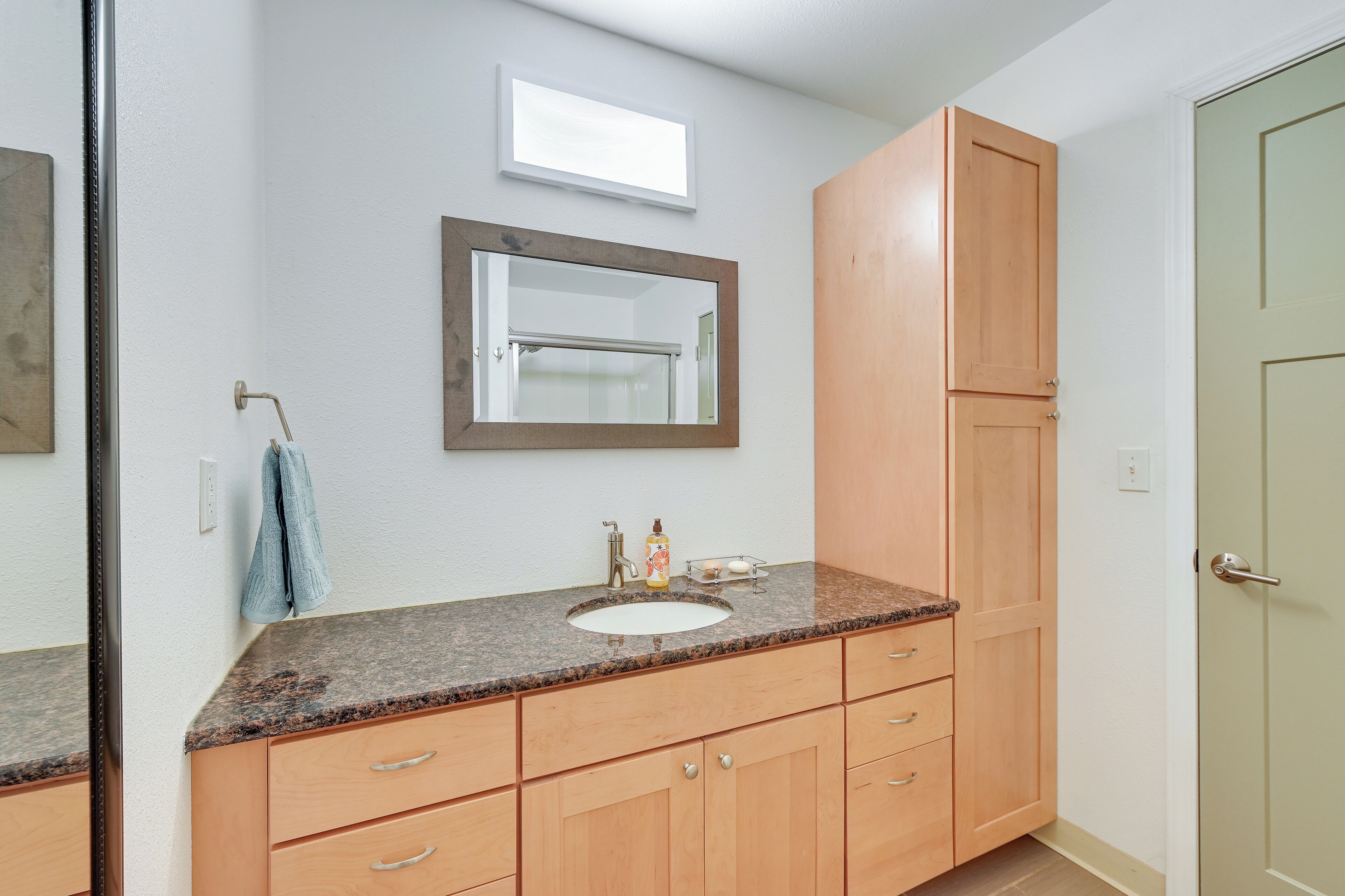A bathroom with a granite countertop sink, wooden cabinets, a towel hanging on the wall, and a mirror.