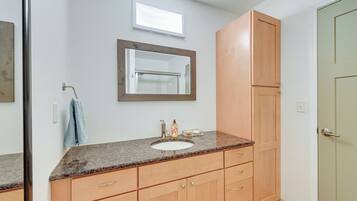 A bathroom with a granite countertop sink, wooden cabinets, a towel hanging on the wall, and a mirror.
