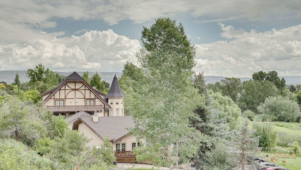A large, traditional house with a prominent tower, surrounded by lush greenery and a clear sky. - Luxe Midway Condo w/ Golf Course & Mountain Views! (Midway)