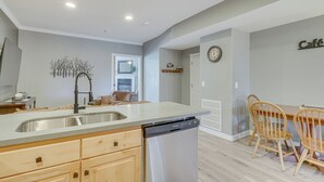 A modern kitchen with a dishwasher, wooden cabinets, and a dining area with a table and chairs. - Luxe Midway Condo w/ Golf Course & Mountain Views! (Midway)