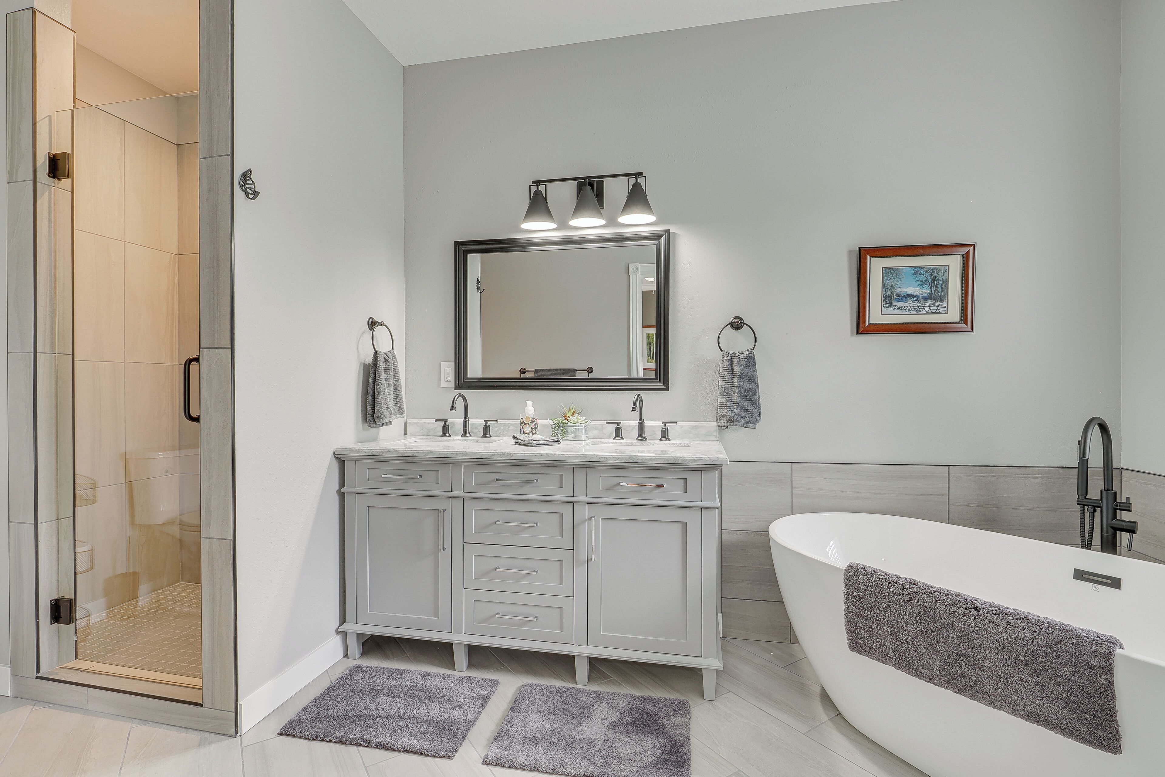 Une salle de bain moderne dotée d’une douche à parois de verre, d’une baignoire sur pieds et d’un meuble-lavabo avec un grand miroir et un éclairage au-dessus.