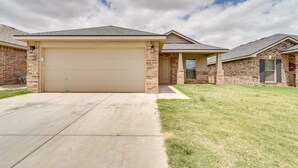 A single-story house with a beige garage door, brick exterior, and a well-maintained lawn. - Pet-friendly Lubbock Home - 10 Mi to Downtown (Lubbock)